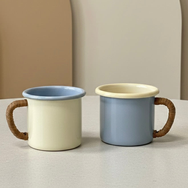 Two pastel enamel coffee mugs with leather-wrapped handles on a neutral background