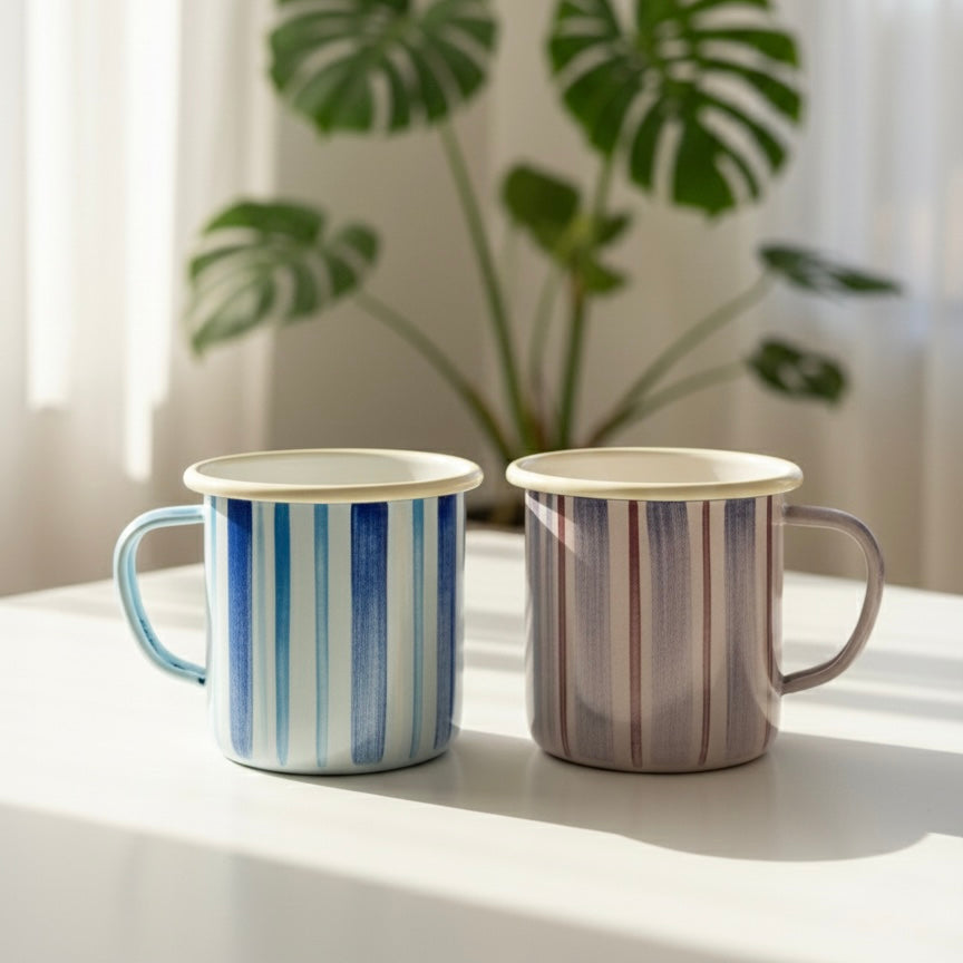 Two striped coffee mugs on a table with a plant in the background