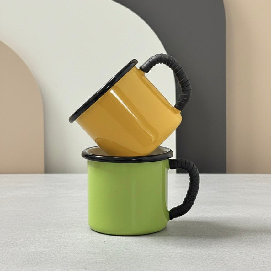 Two stacked enamel mugs, one yellow and one green, on a neutral background.