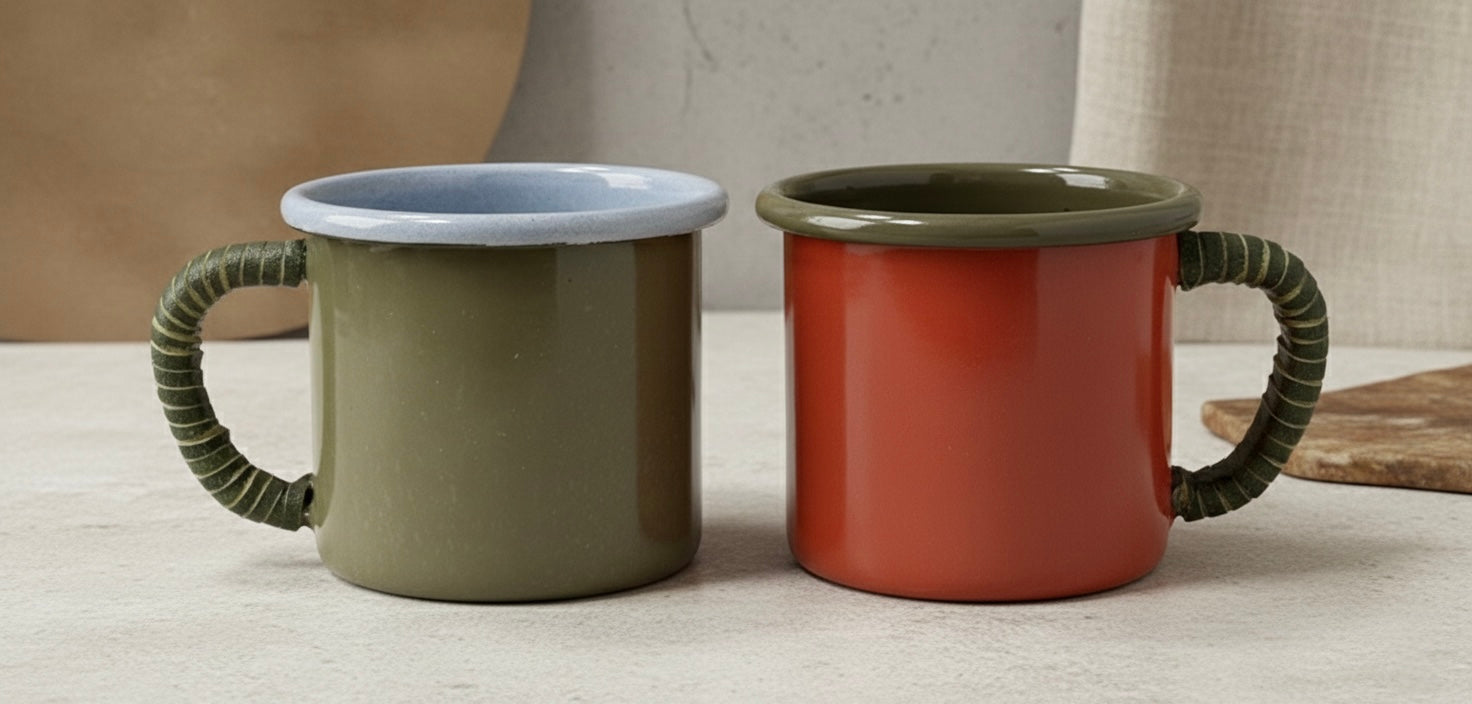 Two enamel coffee mugs, one green and one red, on a light surface with a neutral background.