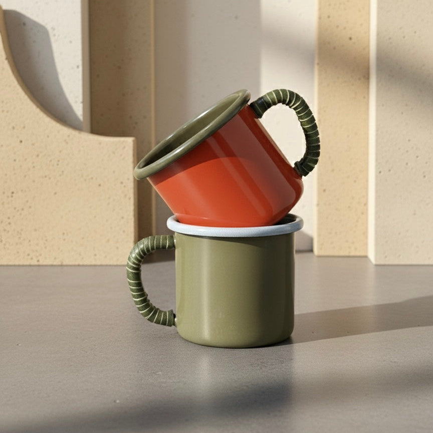 Two stacked enamel coffee mugs in red and green on a neutral background
